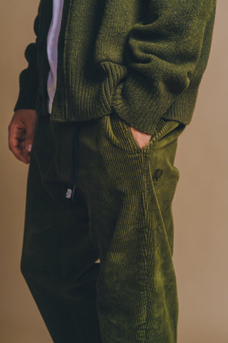 Persona che indossa Corduroy Ecodye Climber Pant in Dark Olive con le mani in tasca | TP_IMAGE_TYPE=MODEL_FRONT