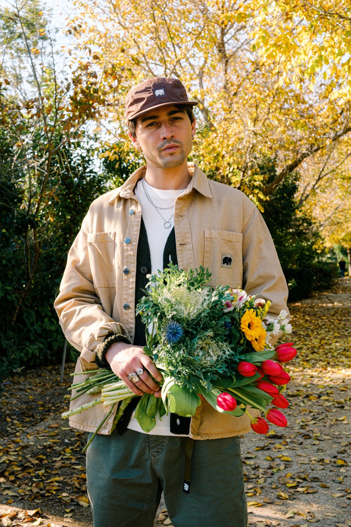Un homme portant une tenue décontractée superposée et tenant un bouquet de fleurs en extérieur | TP_IMAGE_TYPE=LIFESTYLE