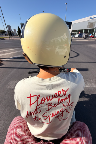 Persona che indossa una Flowers L/S T-Shirt in Antique White e un casco giallo pallido, vista da dietro su una motocicletta con la grafica rossa posteriore visibile | TP_IMAGE_TYPE=LIFESTYLE.