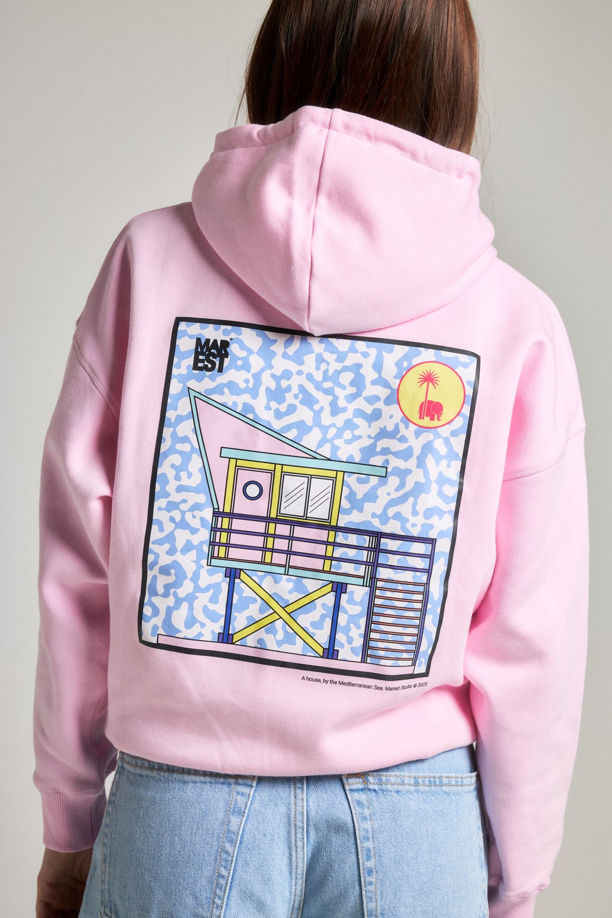 Personne portant un Sweat à capuche oversize Women's Antonyo Marest x Trendsplant en Gum Pink, mettant en valeur un motif graphique vibrant au dos, associé à un bas en jean. | TP_IMAGE_TYPE=MODEL_BACK