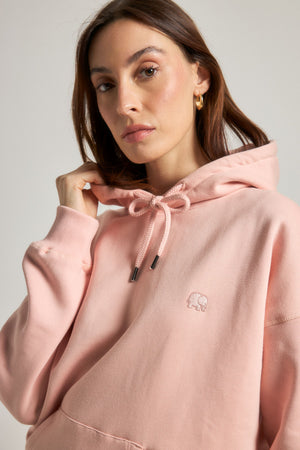 Personne portant un sweat à capuche oversize rose pâle avec cordon de serrage et écusson logo | TP_IMAGE_TYPE=MODEL_FRONT