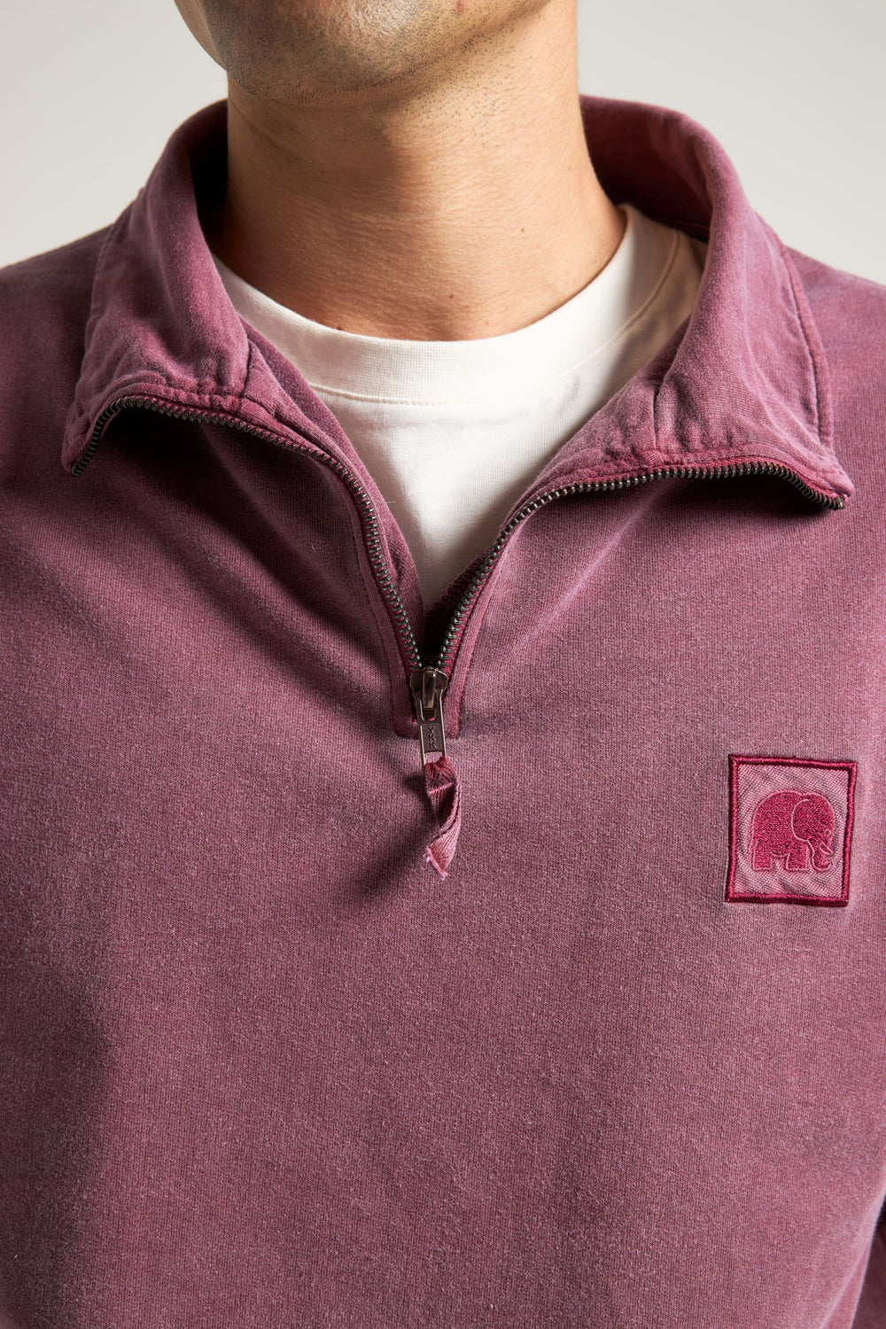 Personne portant un Garnacha Red Sauce Pigment Dyed Quarter Zip Sweatshirt avec un t-shirt blanc en dessous, montrant les détails de la fermeture éclair et du col. | TP_IMAGE_TYPE=MODEL_FRONT