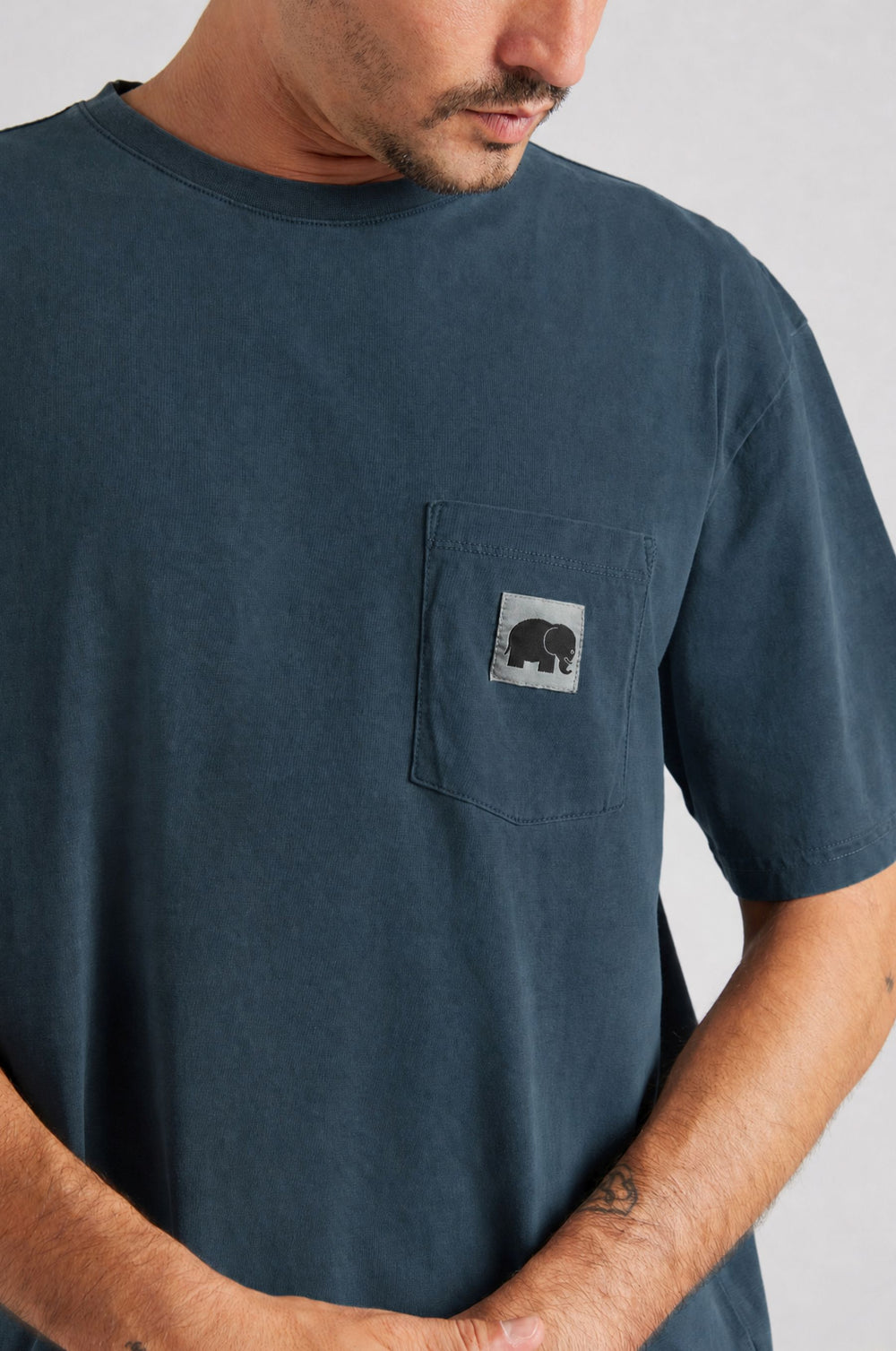 Persona che indossa una camicia a maniche corte blu navy con tasca sul petto decorata con un disegno di elefante, dal fit rilassato e dallo stile casual. | TP_IMAGE_TYPE=MODEL_FRONT
