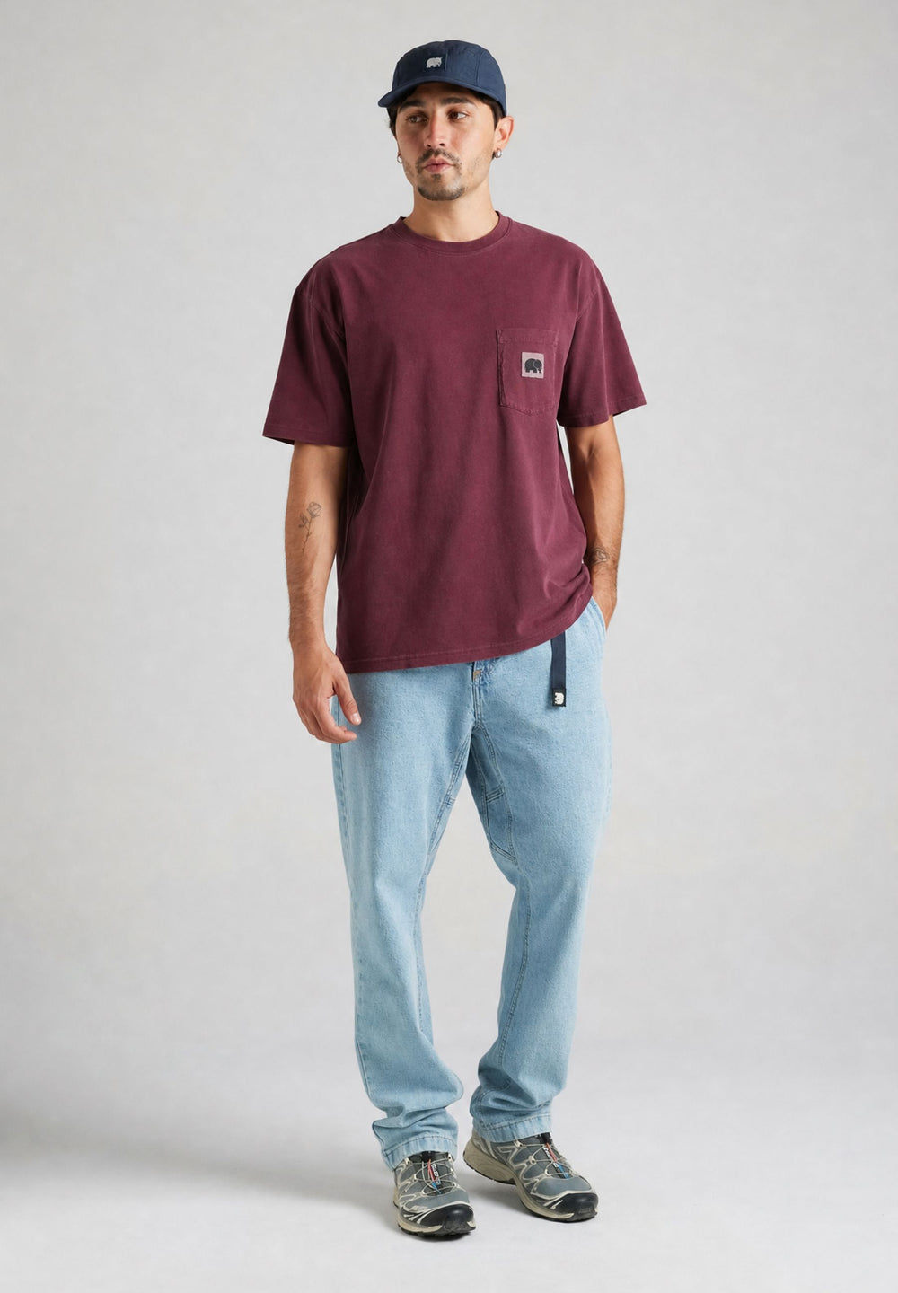Persona che indossa una t-shirt Garza Cabernet con tasca frontale, abbinata a jeans blu chiaro, in piedi su uno sfondo neutro. | TP_IMAGE_TYPE=MODEL_FRONT