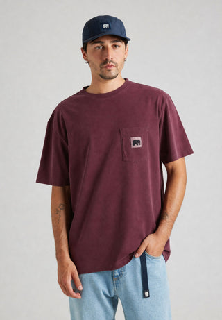 Persona che indossa una t-shirt cabernet con una tasca che riporta il logo di un elefante, abbinata a jeans azzurri e a un cappellino blu navy, in piedi su uno sfondo neutro. | TP_IMAGE_TYPE=MODEL_FRONT