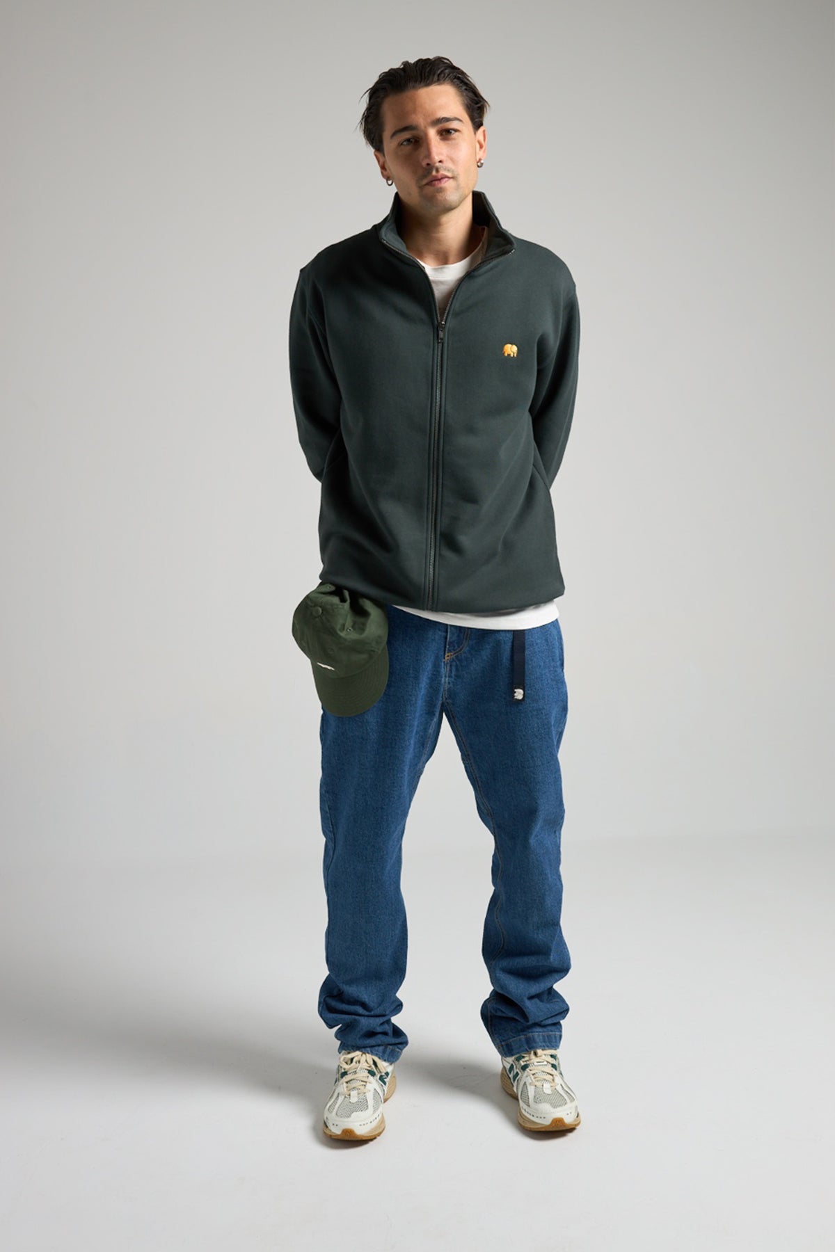 Persona che indossa il Climber Pant in denim riciclato, lavaggio medio, con giacca e berretto verdi | TP_IMAGE_TYPE=MODEL_FRONT