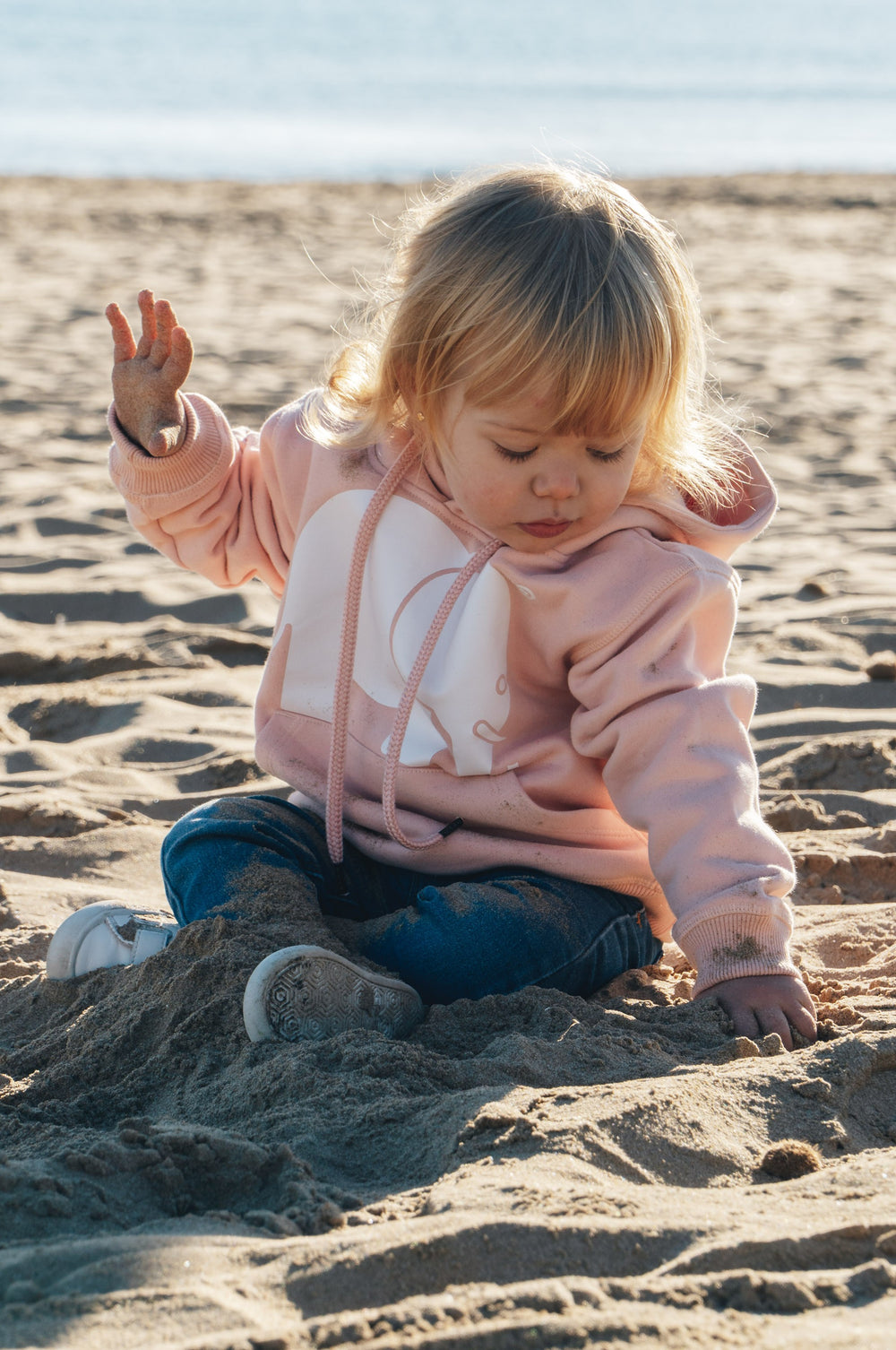 Persona che indossa una Kid's Organic Classic Hoodie Pale Pink mentre gioca nella sabbia | TP_IMAGE_TYPE=LIFESTYLE
