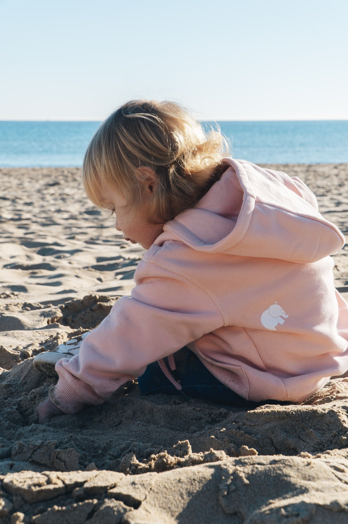 Persona con una Kid's Organic Classic Hoodie Pale Pink che gioca nella sabbia in spiaggia | TP_IMAGE_TYPE=LIFESTYLE